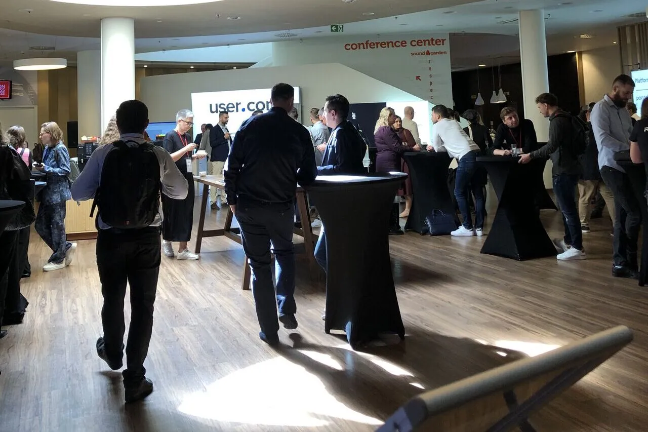 Kuluary konferencji: uczestnicy rozmawiają przy stolikach koktajlowych pod tablicą conference center.