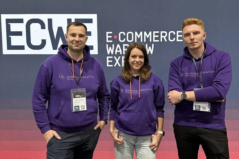 Trzy osoby z Aurora Creation w firmowych bluzach przed ścianką konferencji E‑Commerce Warsaw Expo.